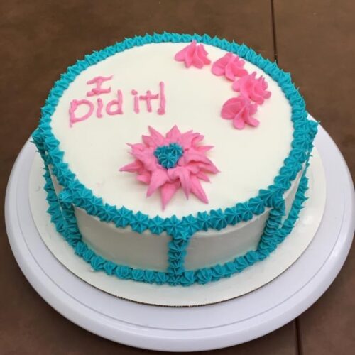 White decorated cake that says "I did it" in pink icing with blue icing decorative edge