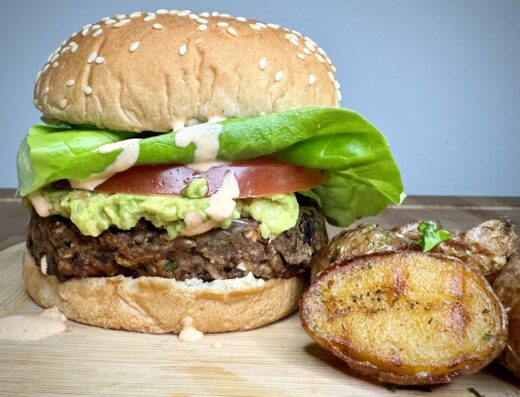 Picture of a thick black bean burger with a sesame bun and crispy potatoes on the side from cooking class